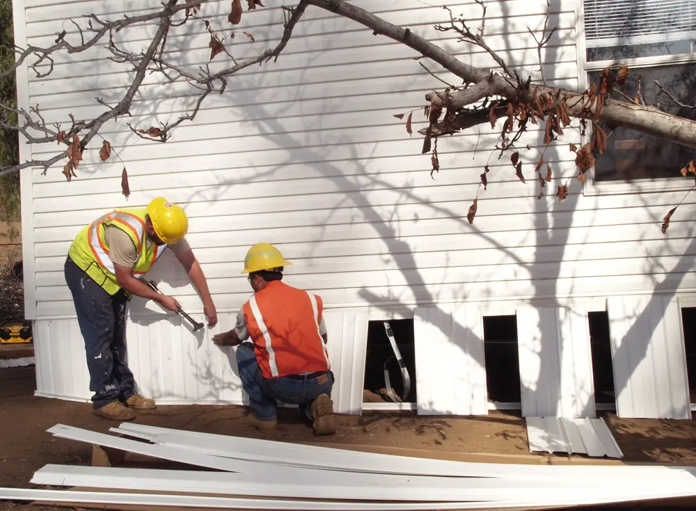 Two workers putting skirting on a manufactured home
